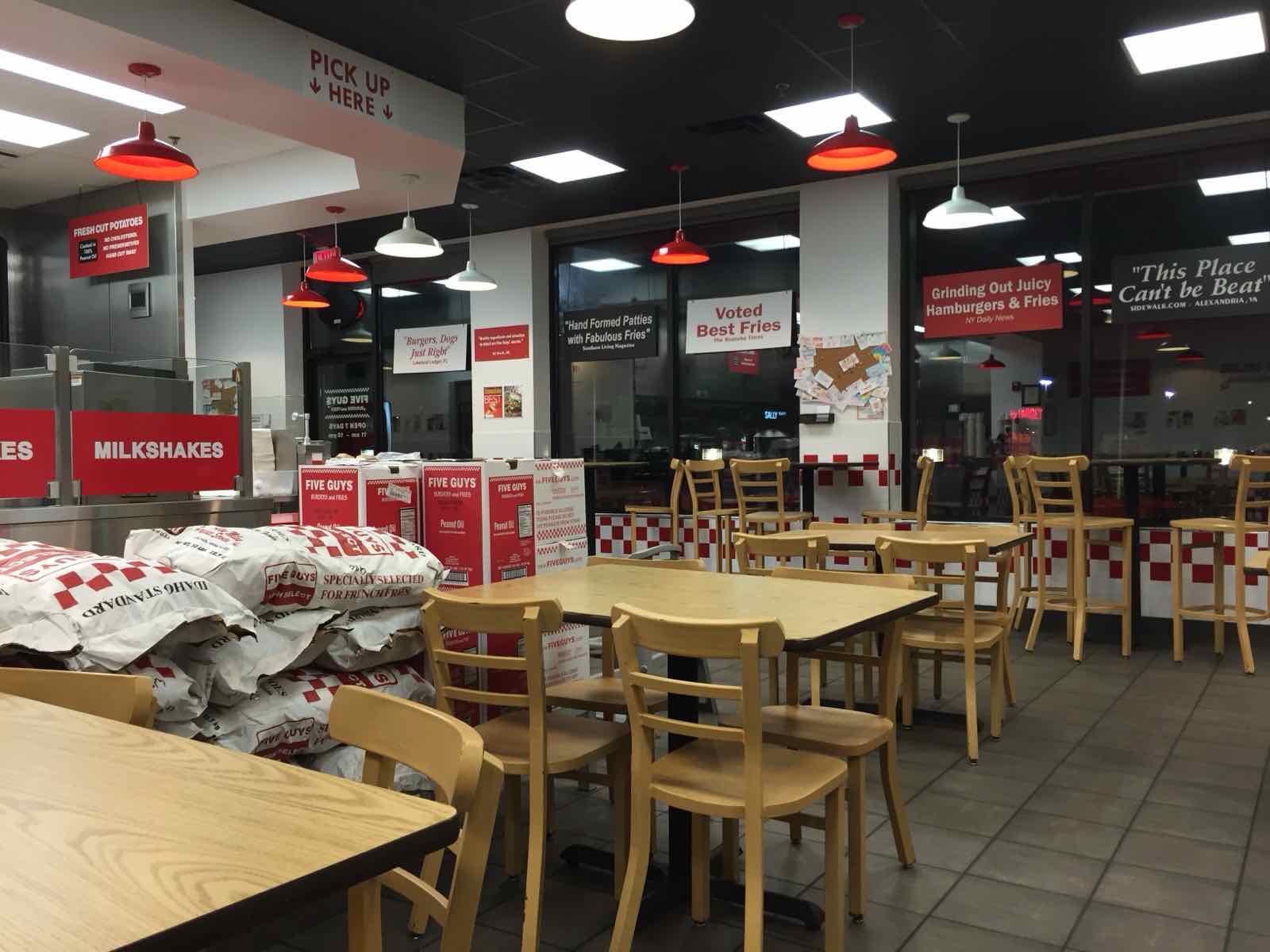 Five Guys interior showing the menu wall with framed press quote signs reading Voted Best Fries, Grinding Out Juicy Hamburgers and Fries, and This Place Can't be Beat