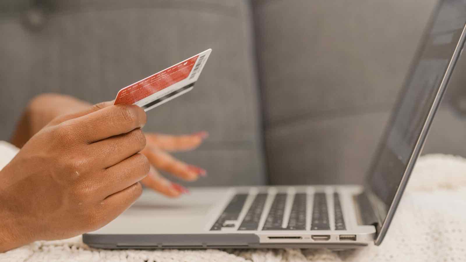 Person holding a red credit card next to an open laptop, illustrating online checkout and secure payment trust signals